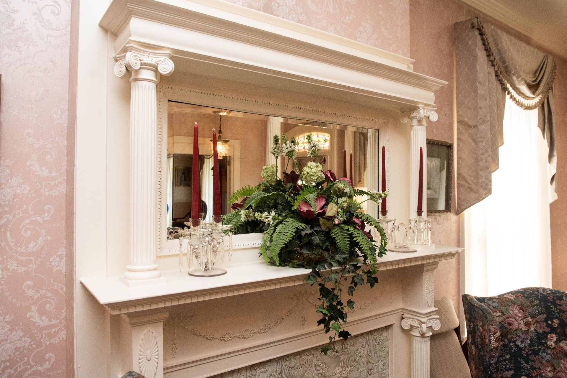 White fireplace with mirror, floral arrangement, and red candles.