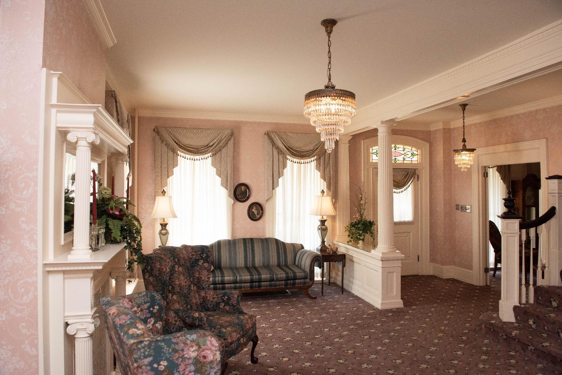 Formal parlor with pink walls, sofa, floral armchair, and a chandelier.
