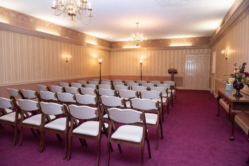 Funeral home chapel with rows of chairs, purple carpet, and decorative walls.