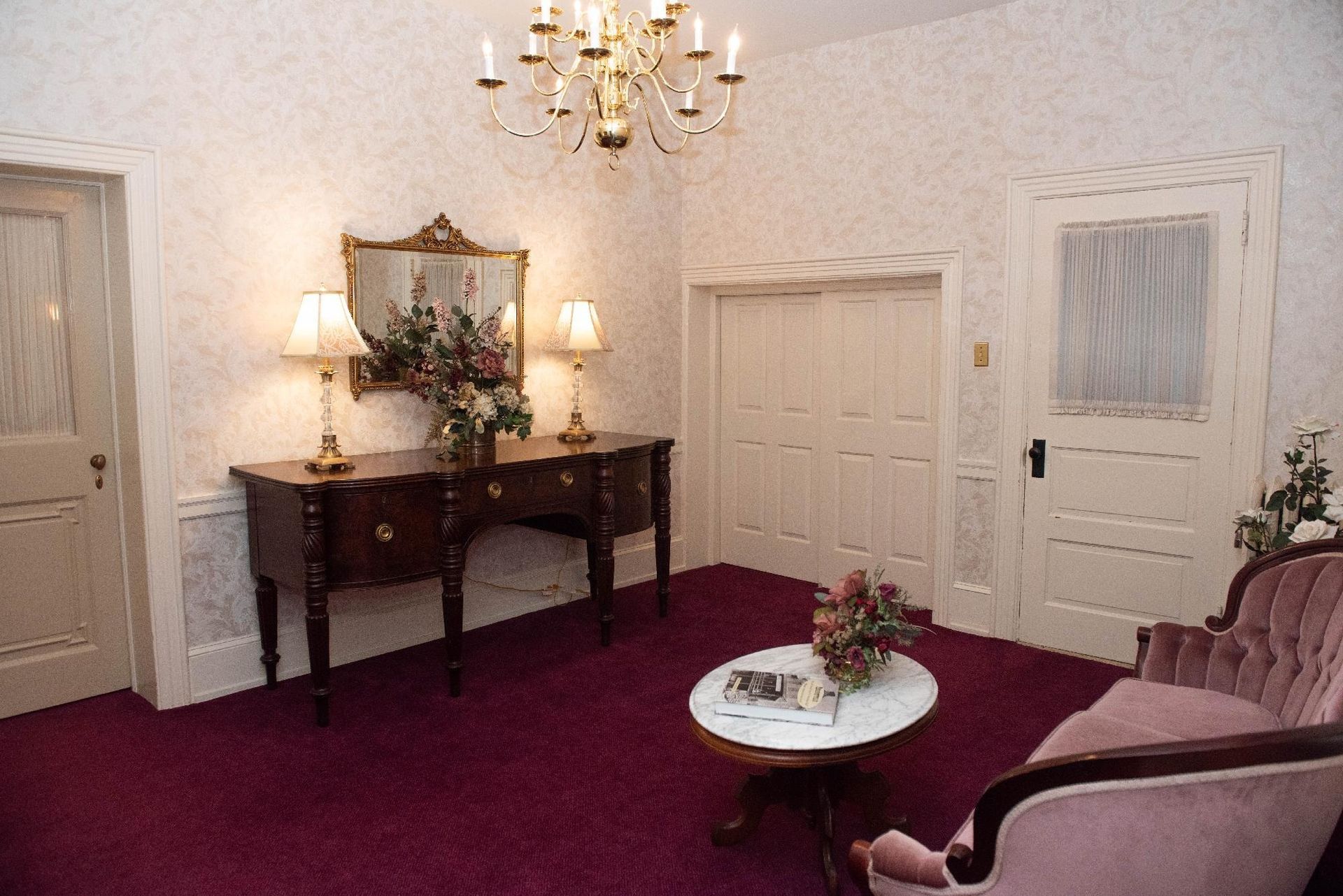 Formal room with dark red carpet, antique furniture, and a chandelier.
