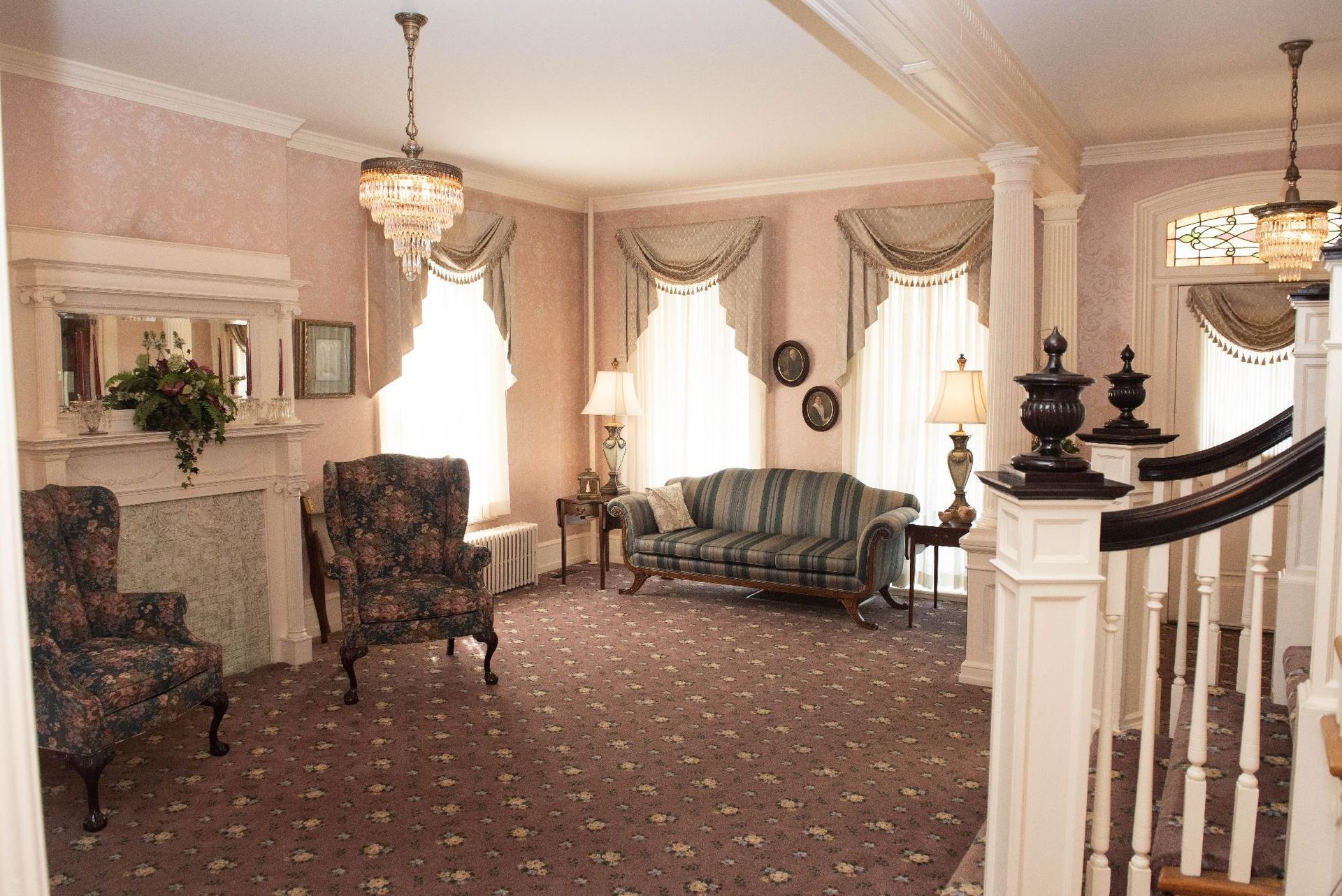 Elegant interior with sofa, chairs, fireplace, and chandelier; muted pink and gold tones.