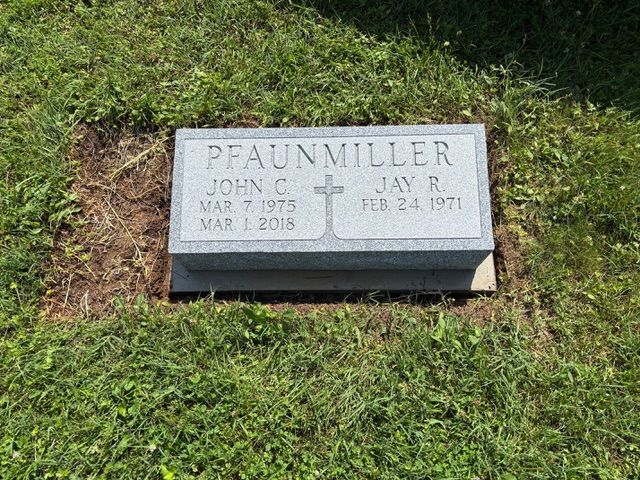 A granite headstone for John C. and Jay R. Pfaunmiller set in a grass cemetery plot.