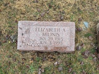 A rectangular, reddish-brown granite headstone for Elizabeth A. Milinis (1915–1995) featuring an etched prayer hands icon.