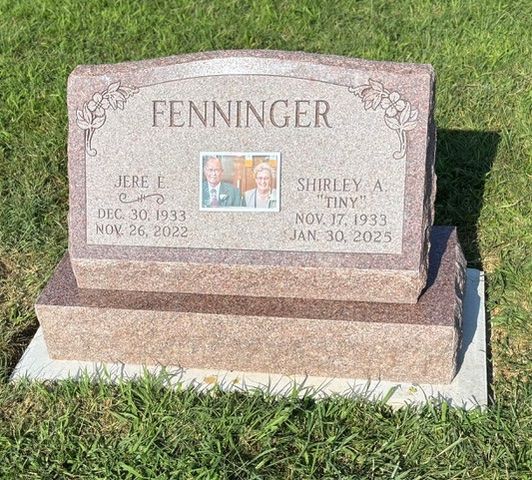 A pink granite Fenninger headstone with a centered photo cameo, placed on a concrete base in a grassy area.