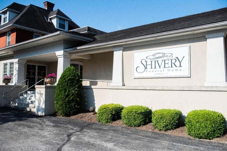 Exterior of Shivery Funeral Home building with sign, cream facade, and manicured shrubs.