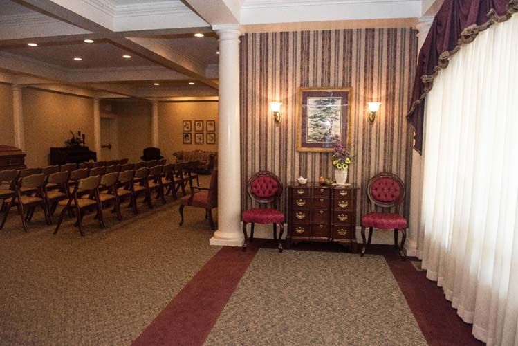 Funeral home interior with seating, columns, a painting, and a draped window.