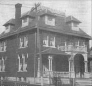 Three-story brick house with dormers, balcony, and porch, likely built in the early 20th century.