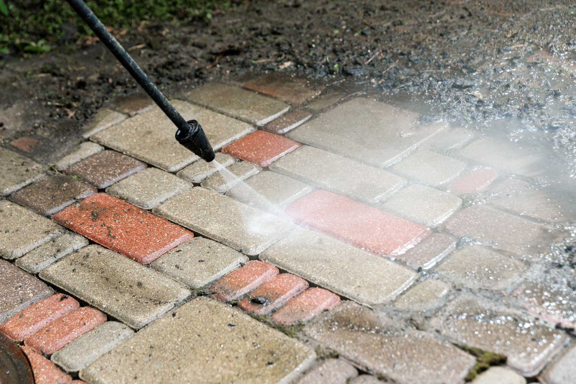 Pressure washer cleaning a brick patio, spraying water across wet paving stones.