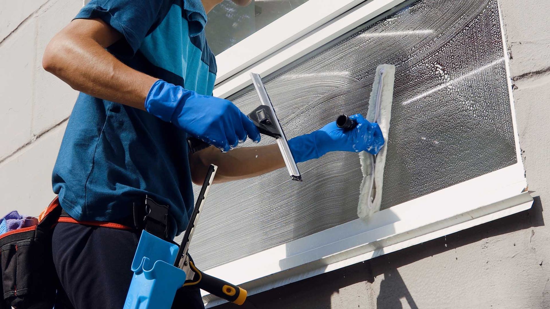 Worker in blue gloves cleaning a window with a squeegee on a building exterior