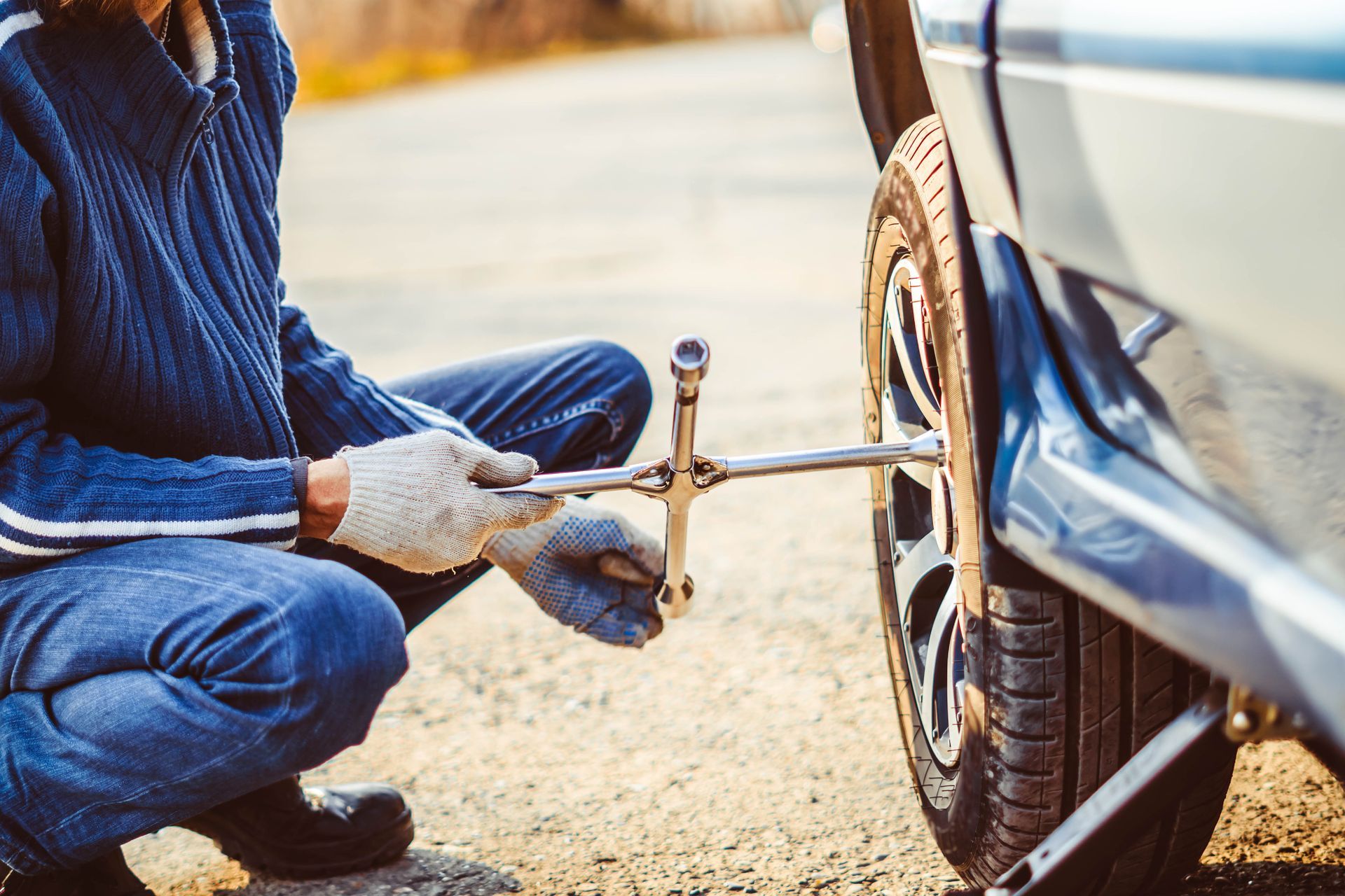Person using a jack to change a car tire on a roadside.