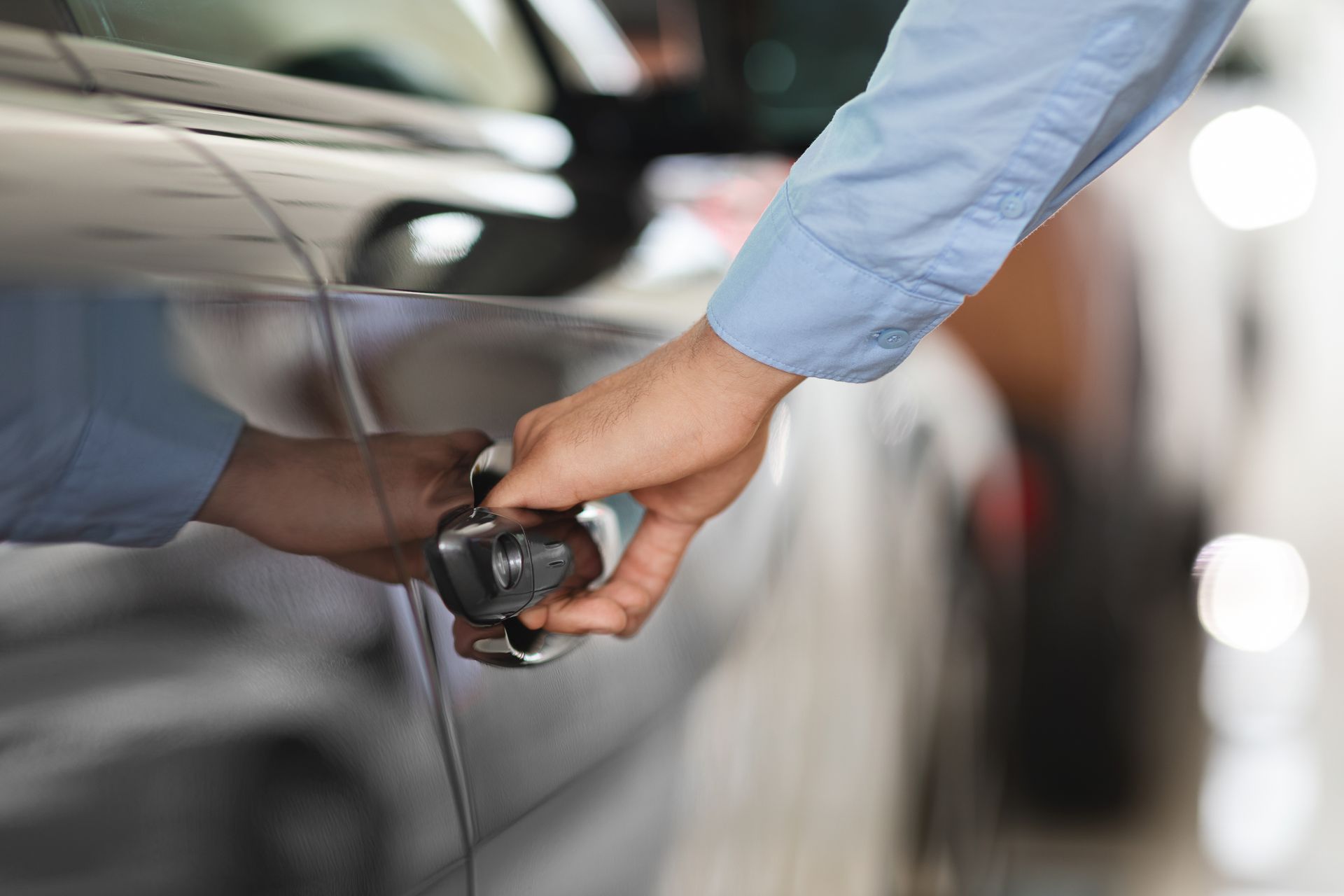 Hand handing car keys to another person beside a silver car