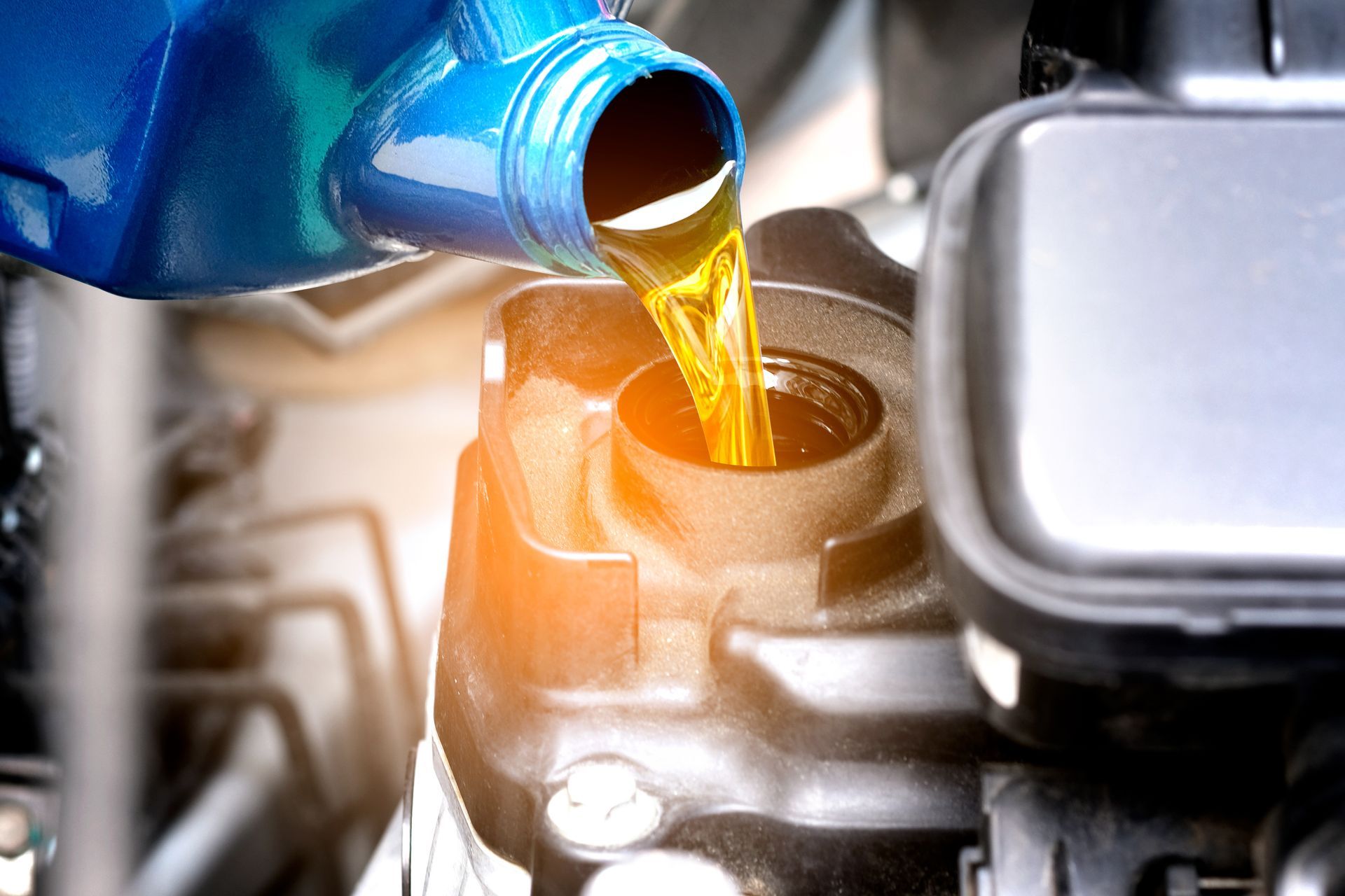 Pouring golden motor oil from a blue container into an engine fill cap