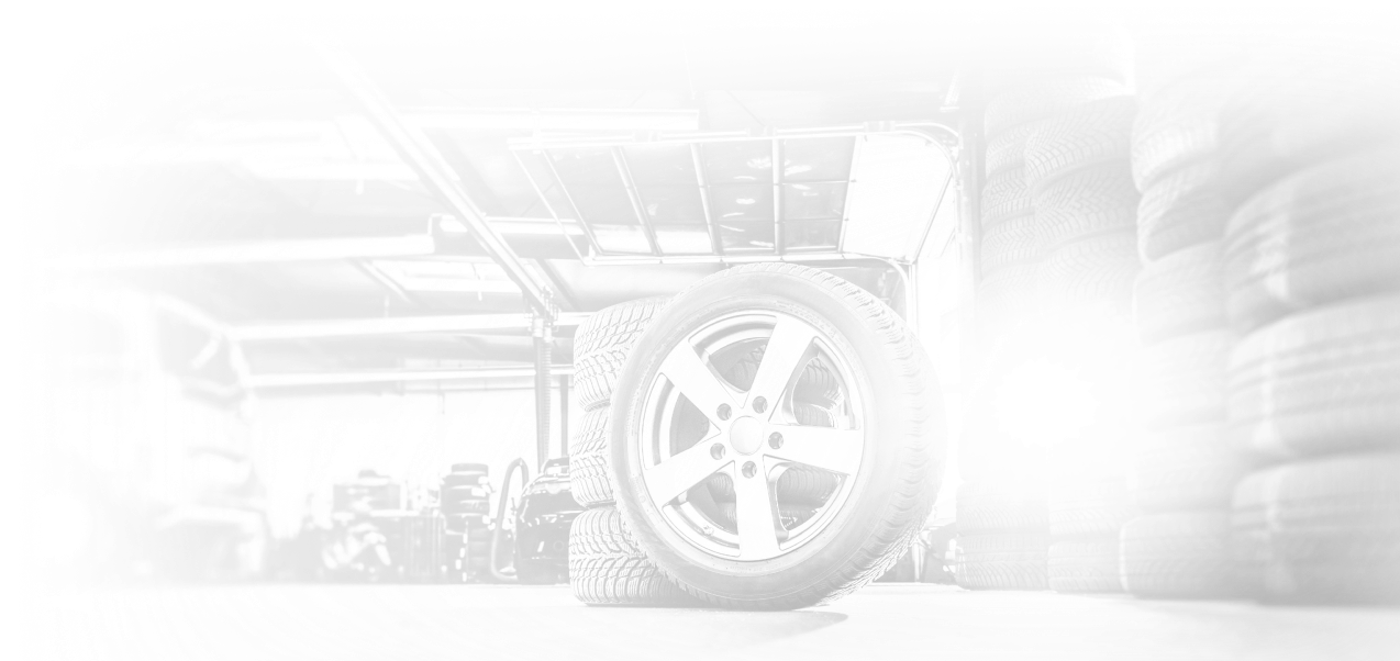 Car tire on a lift in an auto shop, with stacks of tires on the right.