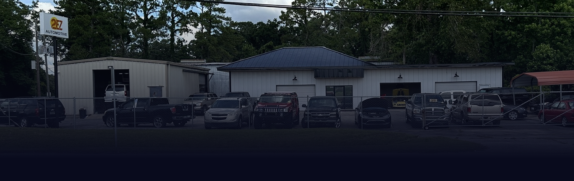 Parking lot outside a small building with parked cars and a sign on a post.