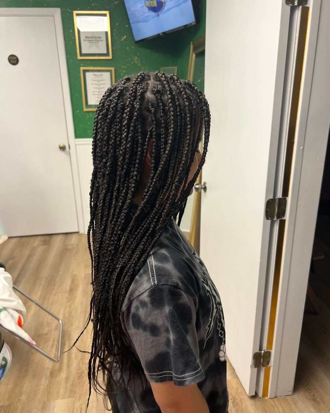 Side view of a person with long braided hair standing indoors in a hallway.