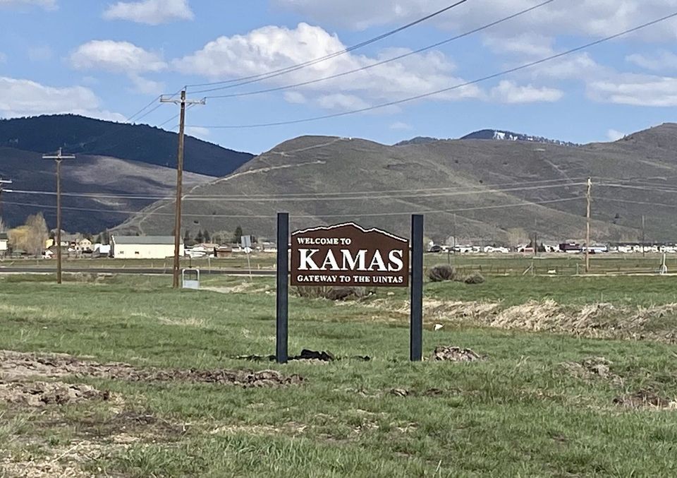A sign that says kamas in a field with mountains in the background
