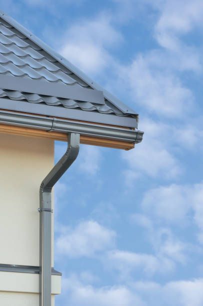 Gray rain gutter along the edge of a house roof, blue sky background.