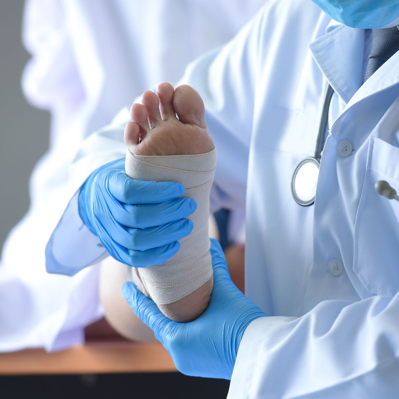 Healthcare worker wrapping a patient's foot with a white bandage, wearing blue gloves and a white coat.
