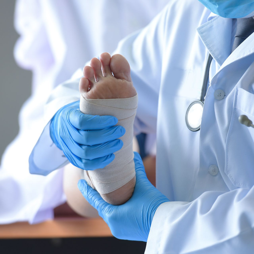 A diabetic podiatrist wrapping a patient's foot with a white bandage, wearing blue gloves and a white coat.