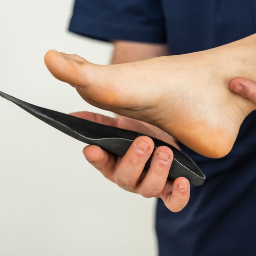 Foot being examined by a custom orthotics specialist with a black insole in hand, suggesting a foot support fitting.