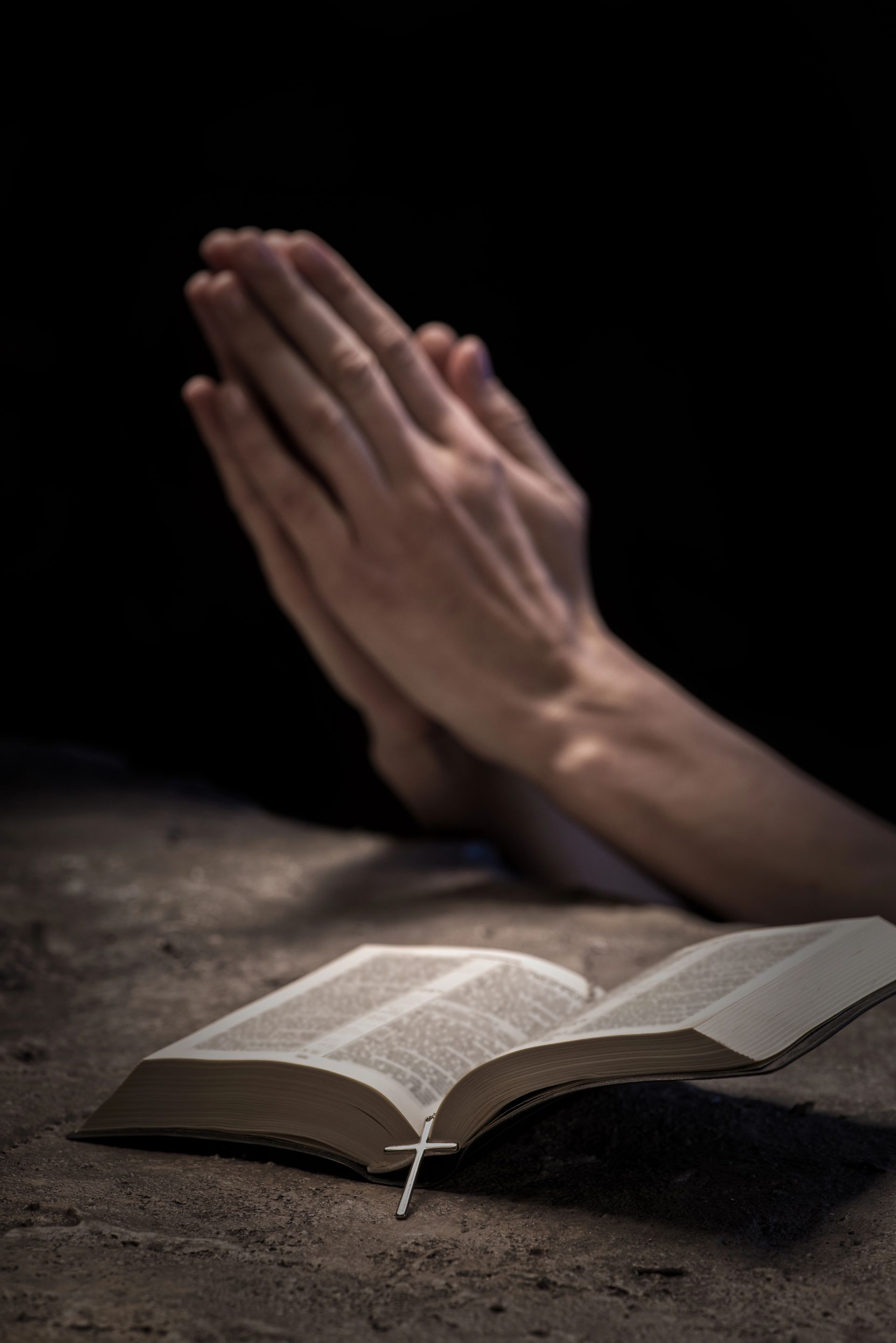 Una persona está orando con las manos juntas sobre una Biblia abierta.