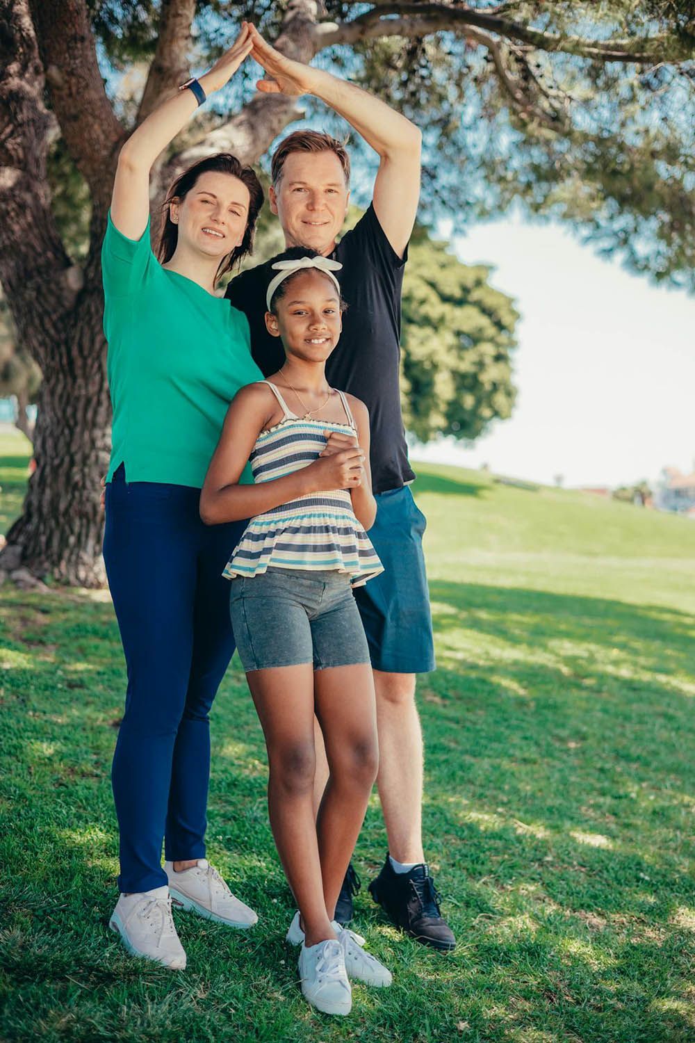 A family is making a heart shape with their hands in a park.