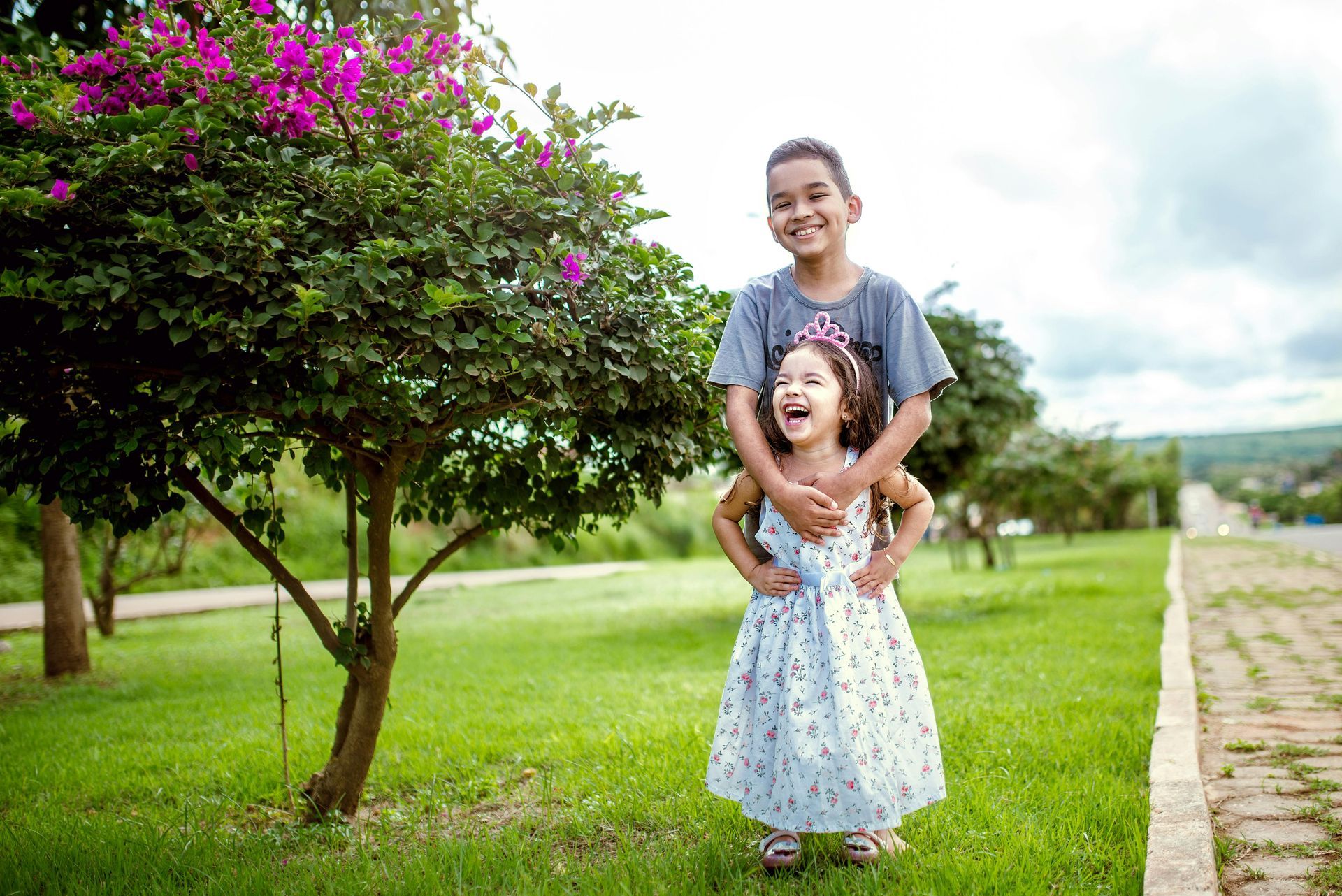 A boy and a girl are standing next to each other in a park.