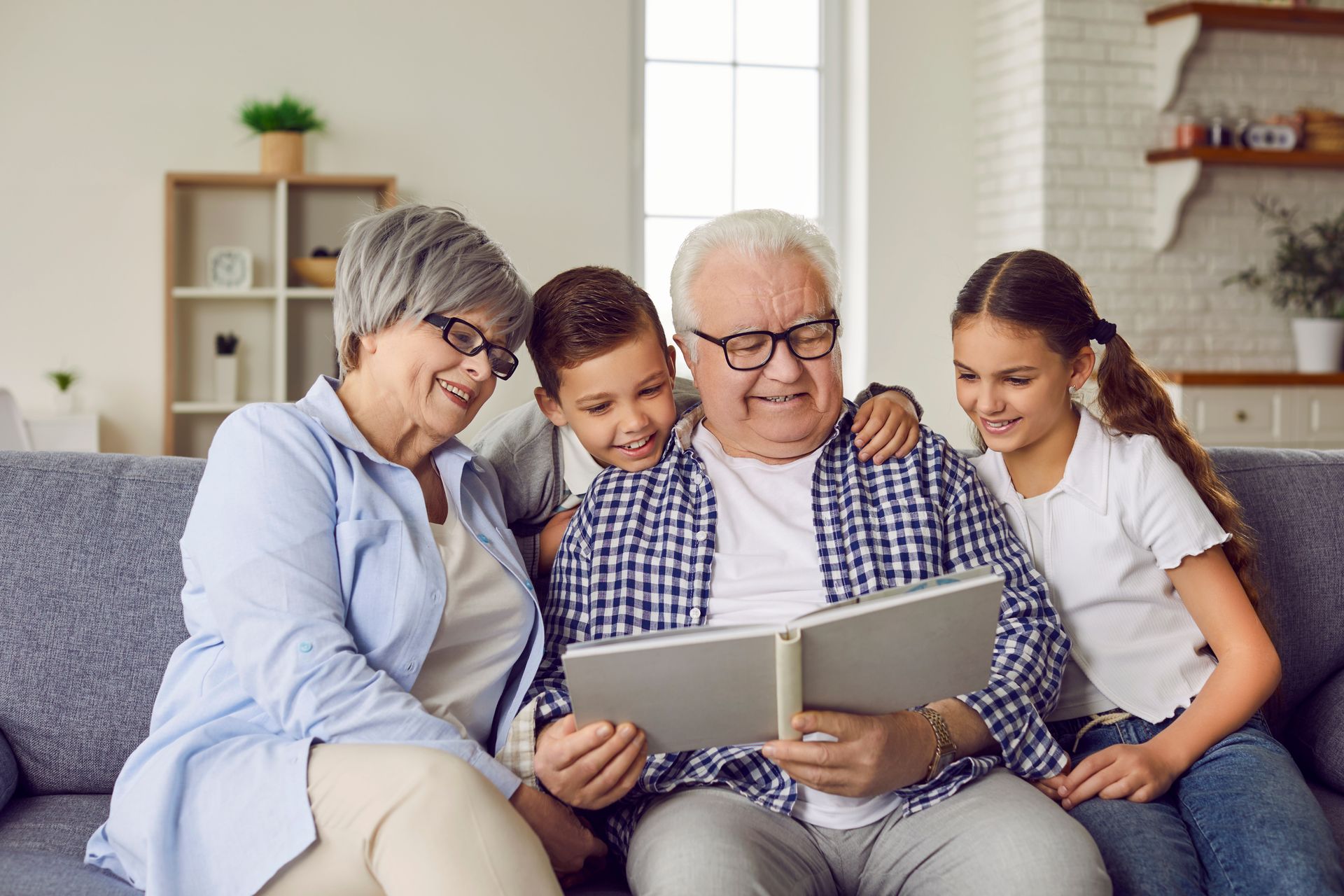 Four people sharing a photo album on a couch in a bright living room