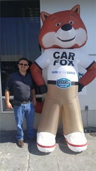 Man standing beside a giant Car Fox mascot statue outside a dealership | A-Tech Auto Repair