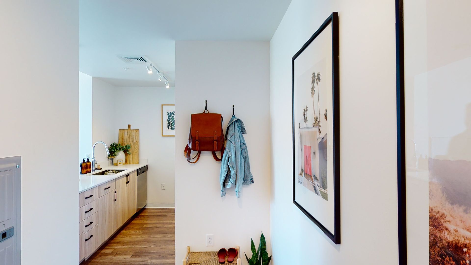 A hallway with a picture on the wall and a backpack hanging on the wall.