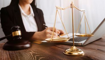 Legal desk scene with a gavel, brass scales, and a person writing on a laptop