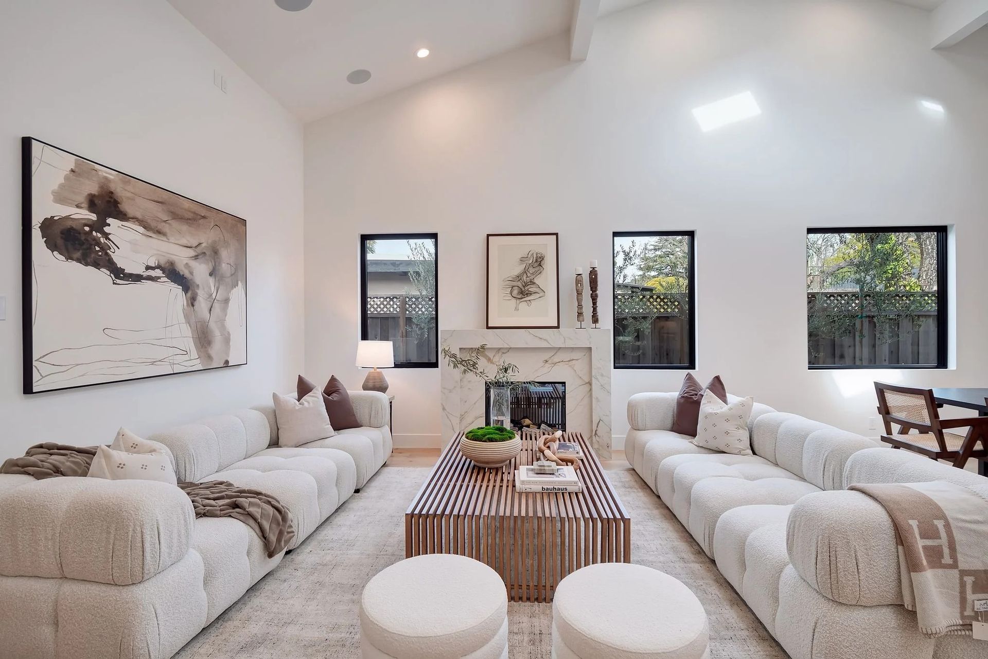 Living room with white sofas, marble fireplace, artwork, and a striped coffee table.