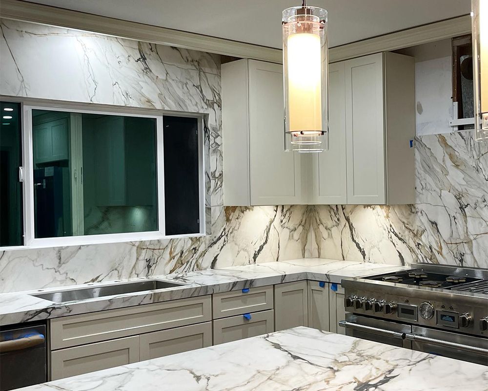 Modern kitchen with marble countertops and backsplash, light cabinets, and a stainless steel range.