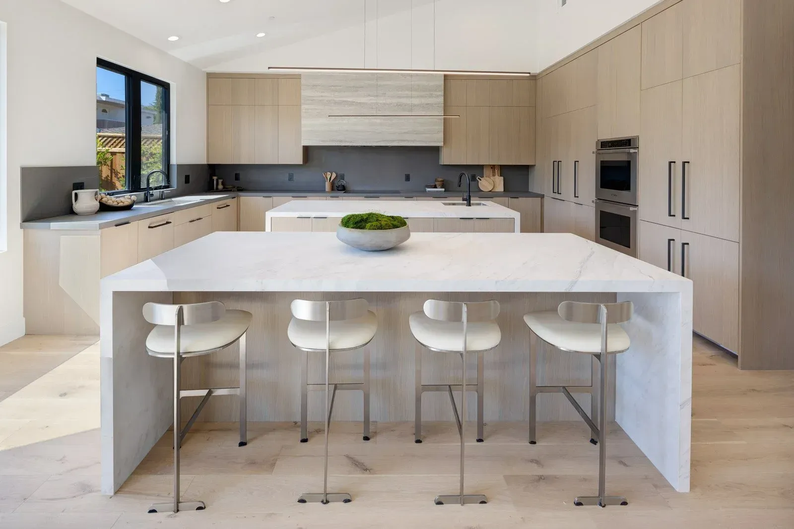 Modern kitchen with light wood cabinets, white countertops, and four bar stools.