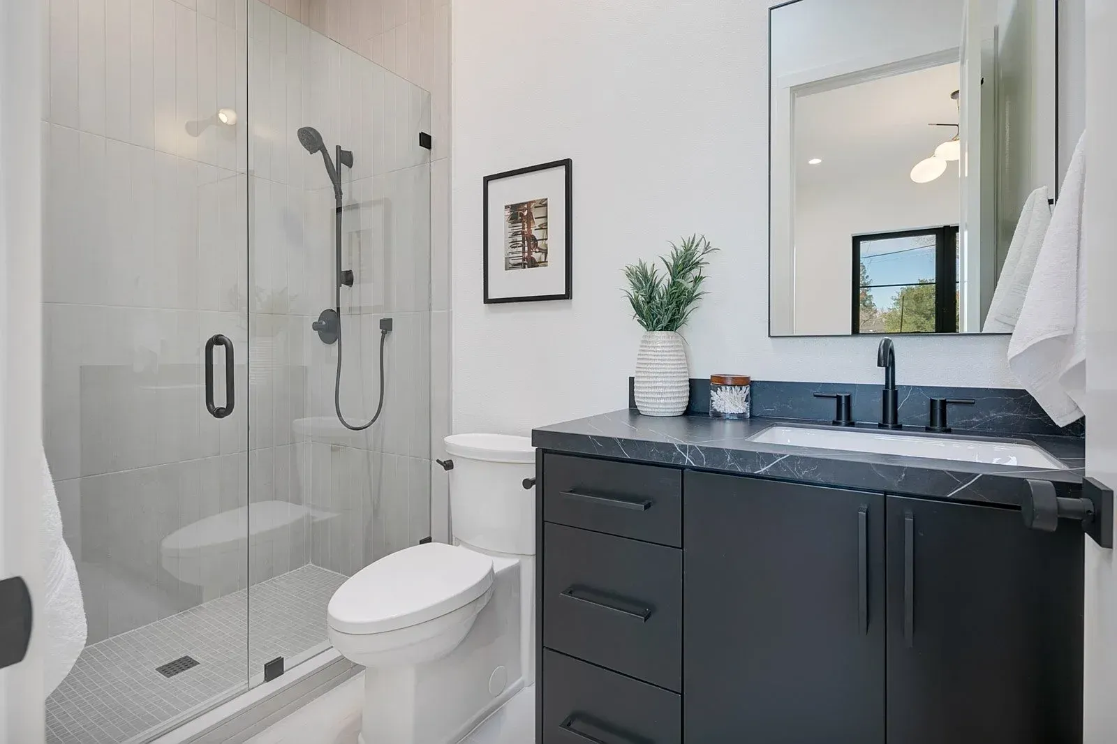 Modern bathroom with a glass shower, dark vanity, toilet, and white walls.
