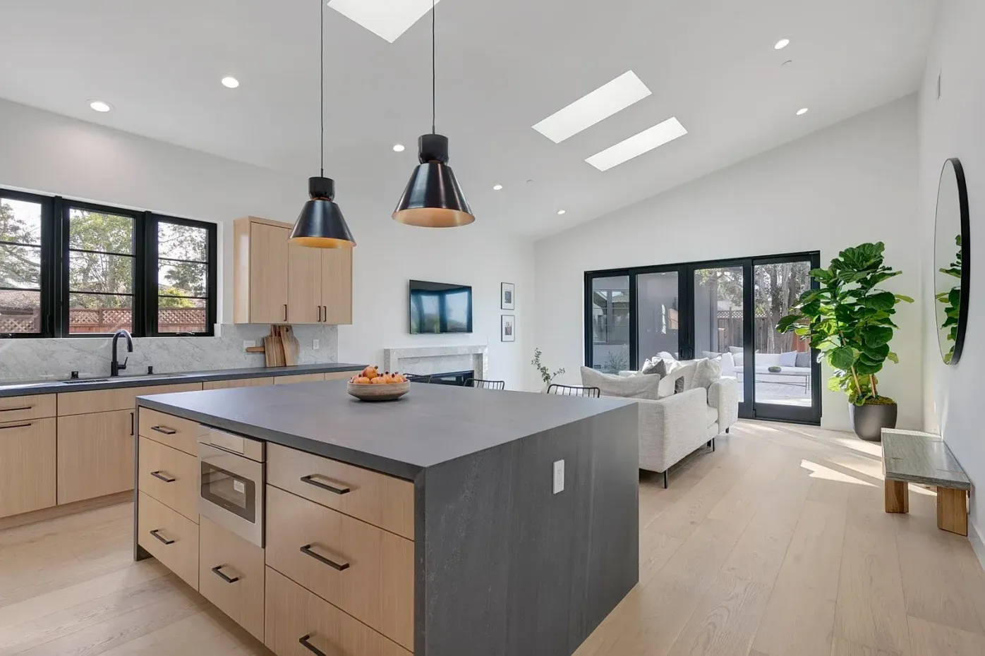 Modern kitchen with island, pendant lights, stainless steel hood, light wood cabinets.