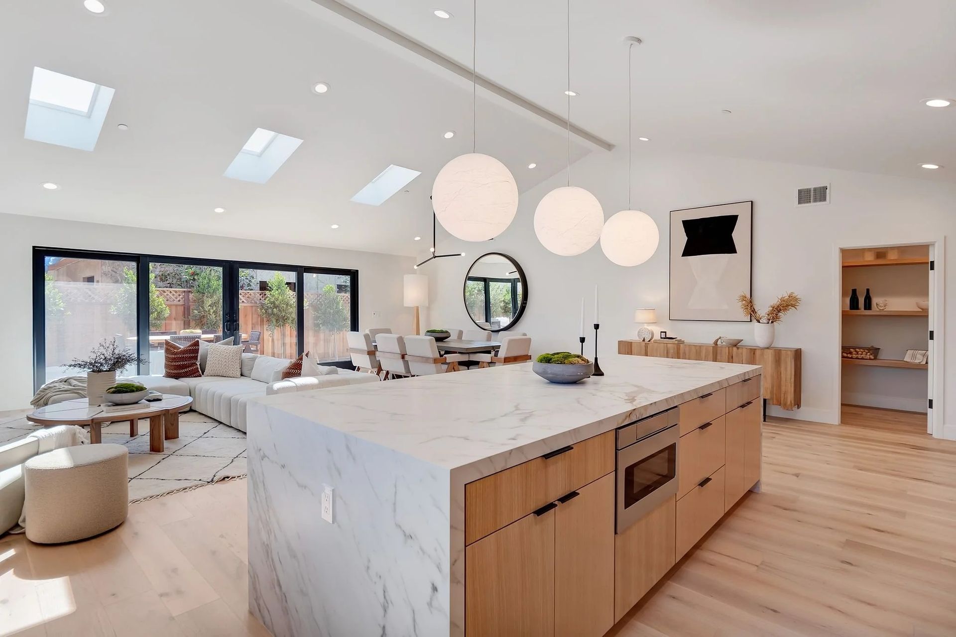 Open-concept kitchen with marble island, wood cabinetry, and light fixtures. Living area with sofa, and skylights.