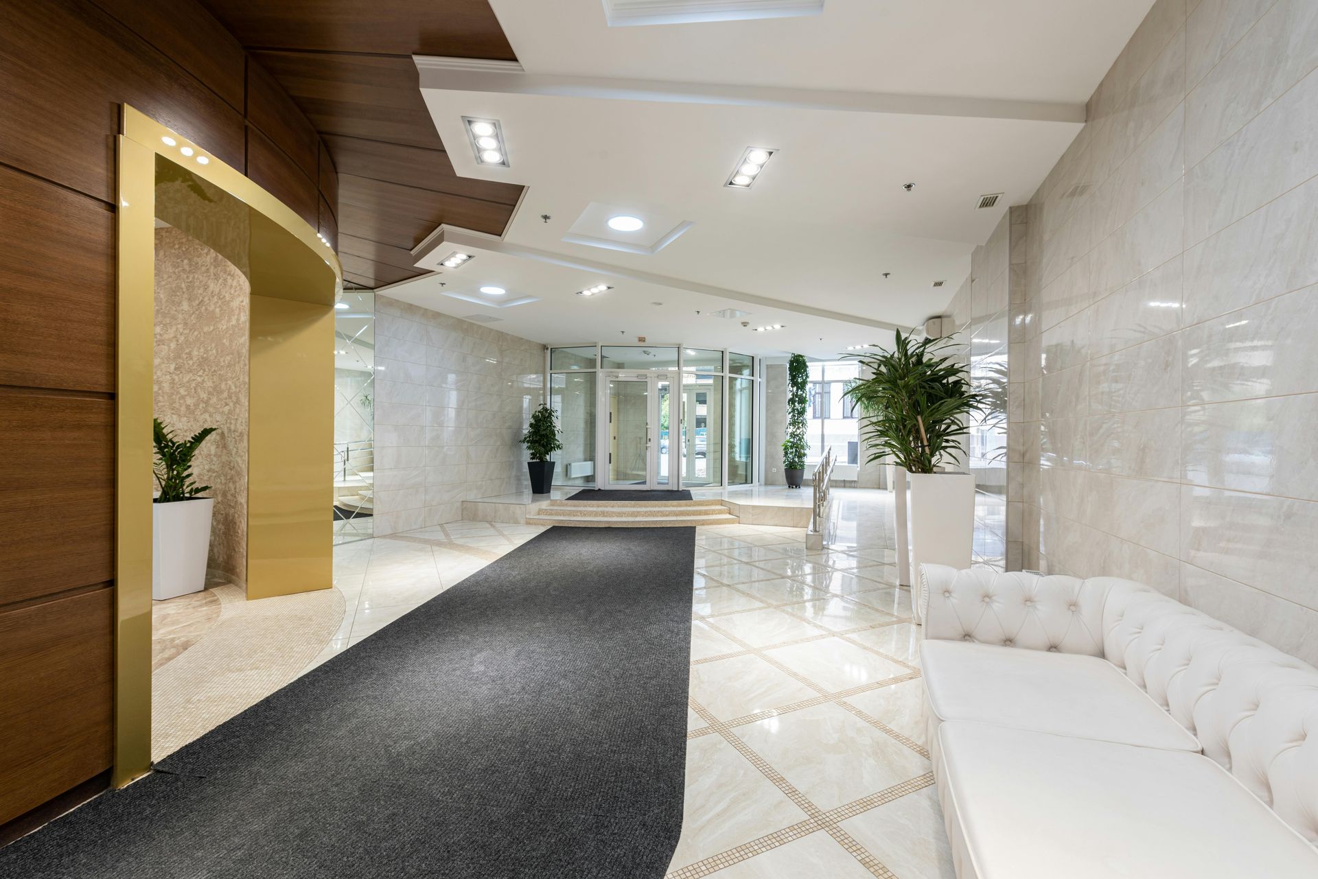 Elegant lobby with white tiled walls, black carpet, gold trim, and a white couch.