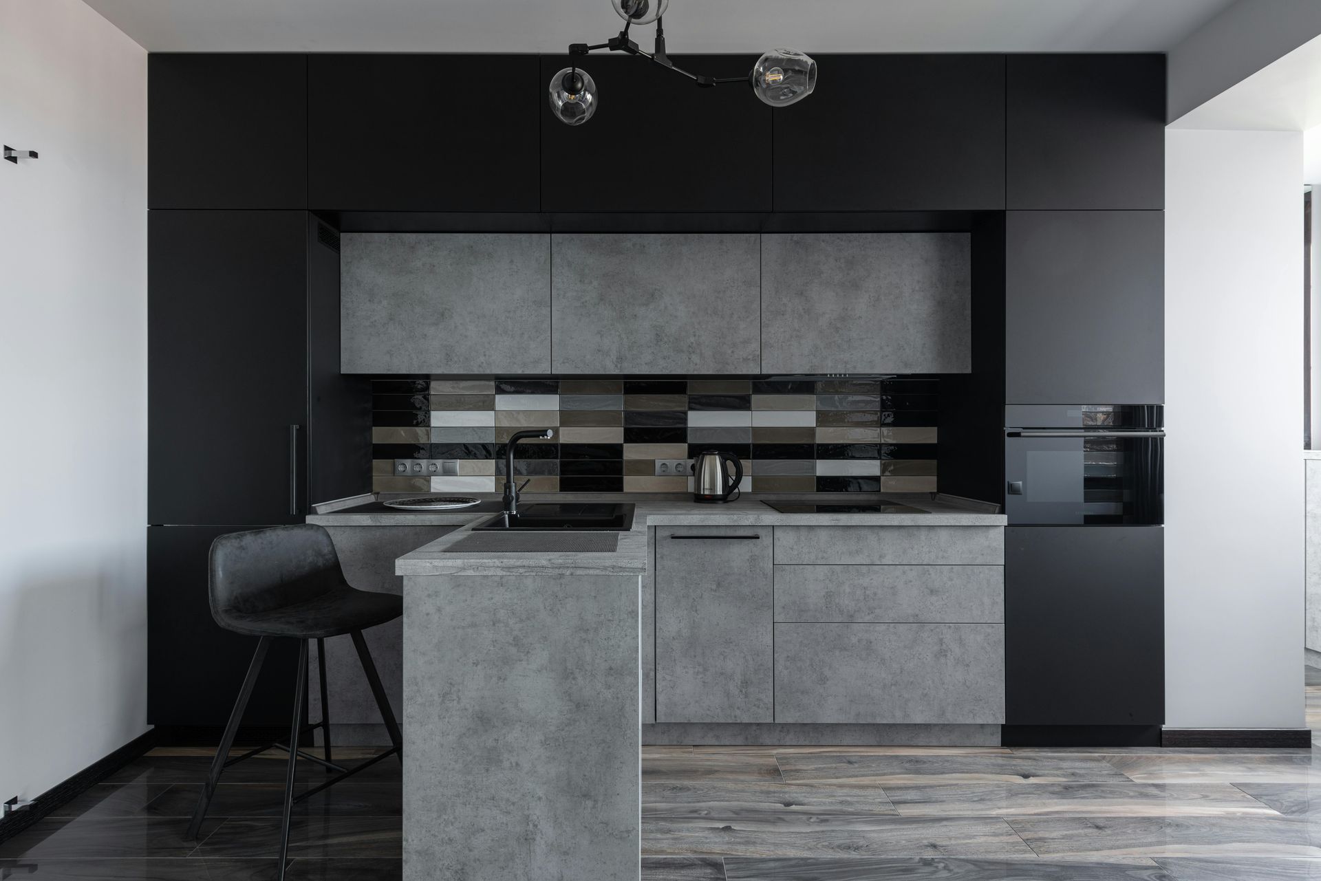 Modern kitchen with black and gray cabinets, concrete countertops, and a breakfast bar.