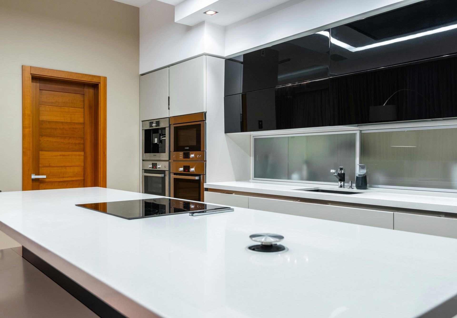 Modern kitchen with white island, stainless steel appliances, and brown wooden door.