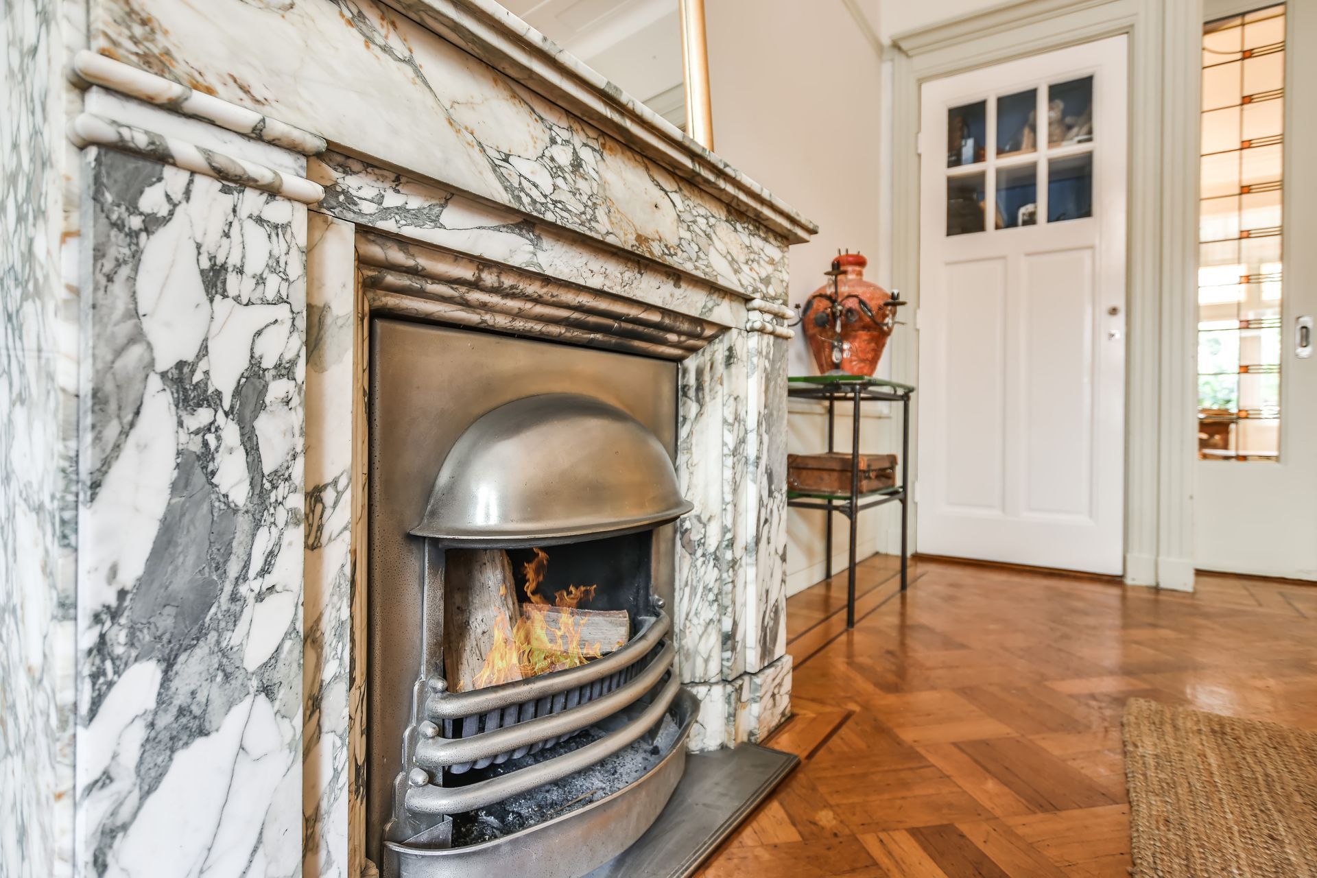 Marble fireplace with fire burning, adjacent to a white door and wood floor.