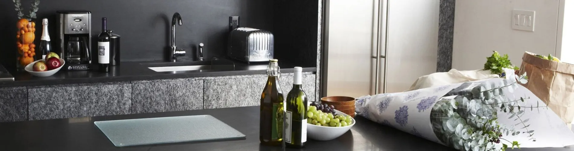 A kitchen with a bottle of wine and a bowl of grapes on the counter.