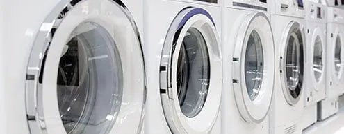 A row of white washing machines are lined up in a laundromat.