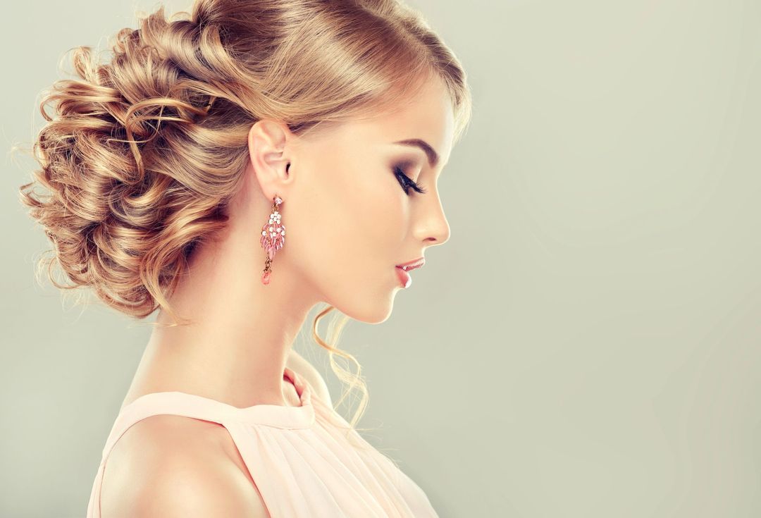 Profilo di una donna con un'elegante acconciatura raccolta e orecchini rosa su uno sfondo beige tenue.