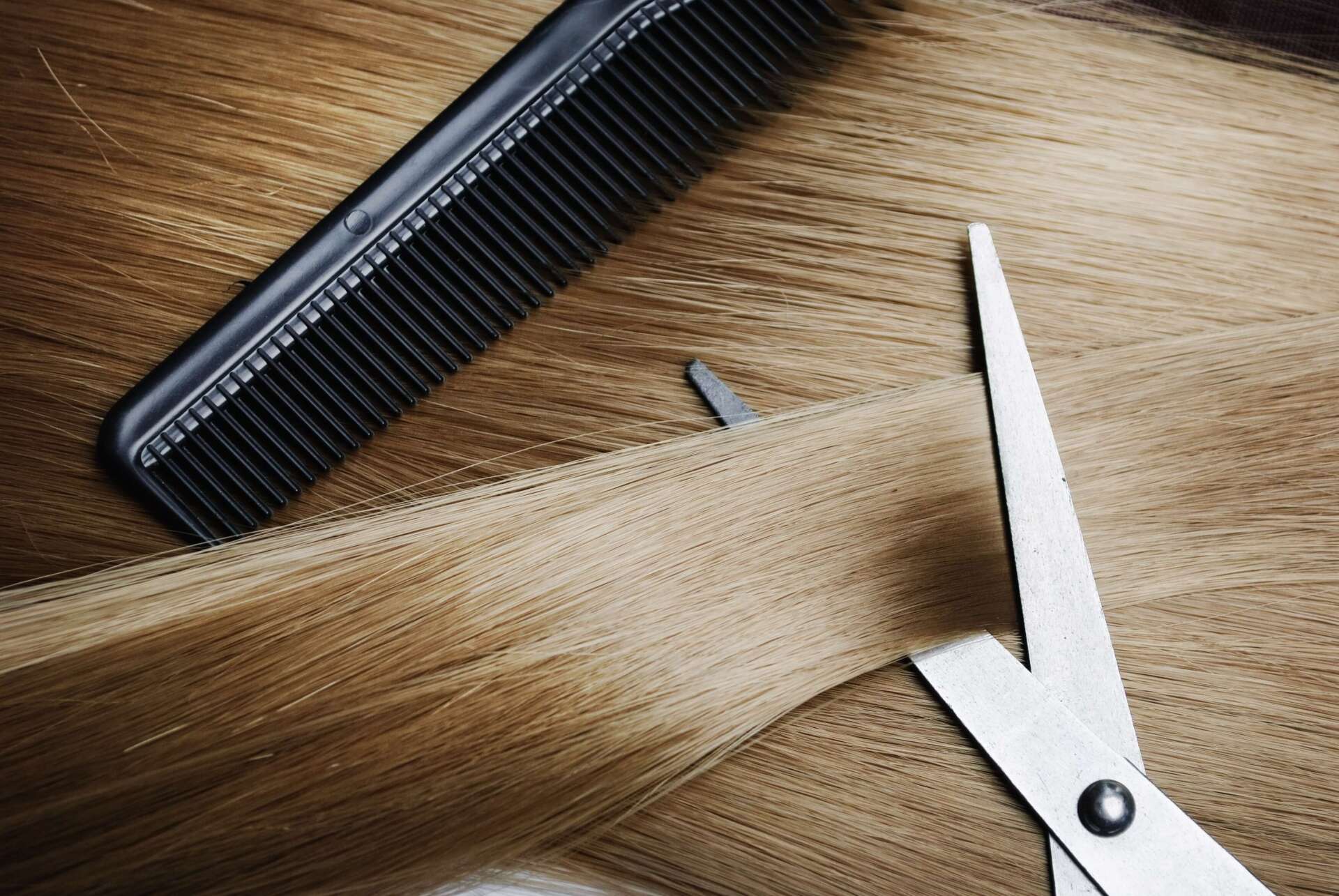 Capelli tagliati con forbici bianche accanto a un pettine nero su una superficie di legno.
