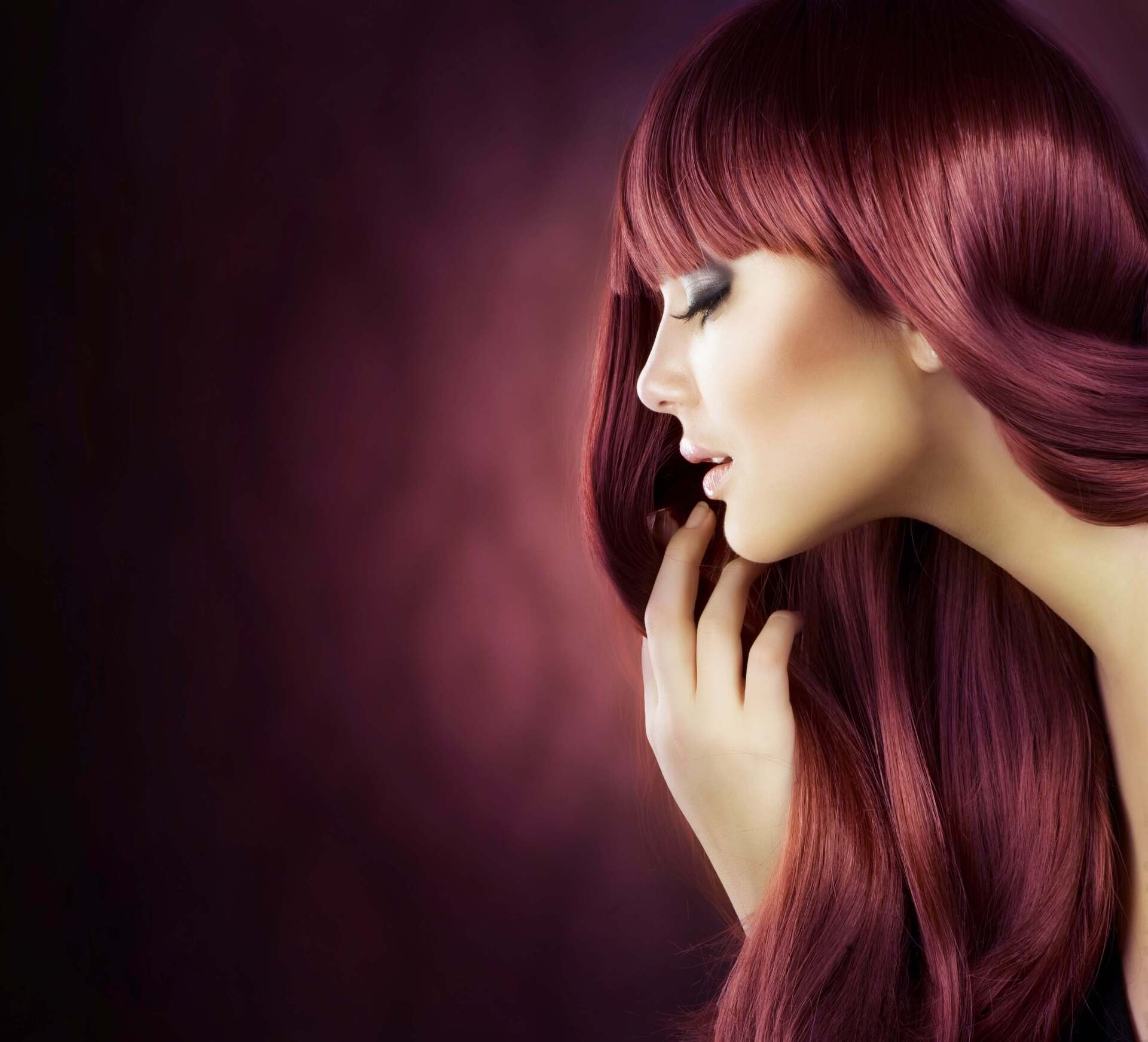 Profilo di una donna con lunghi capelli color bordeaux su sfondo viola scuro.