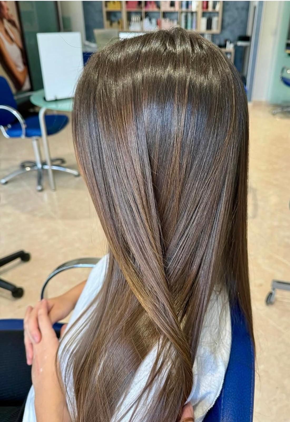 Lunghi capelli castani, lisci e setosi, raccolti in una mezza treccia su una poltrona da parrucchiere.