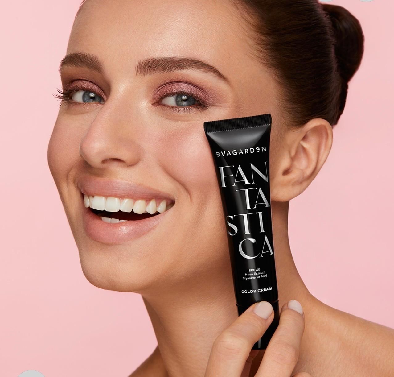 Donna sorridente che tiene in mano un tubetto di prodotto di bellezza nero su sfondo rosa