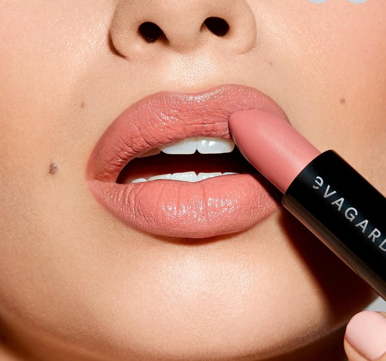 Primo piano di labbra che applicano rossetto rosa nude con un tubetto di trucco.