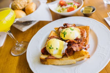 Eggs Benedict on toast with bacon, a side salad, bread rolls, and a glass of orange juice on a wooden table. Eggs Benedict on toast with bacon, a side salad, bread rolls, and a glass of orange juice on a wooden table.